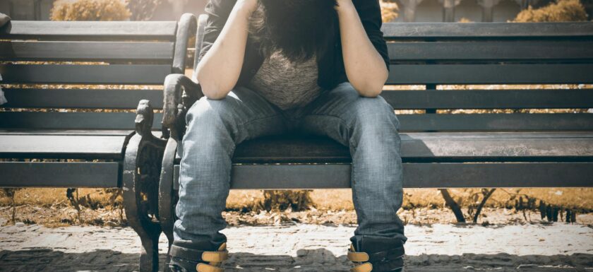 man in black shirt and gray denim pants sitting on gray padded bench